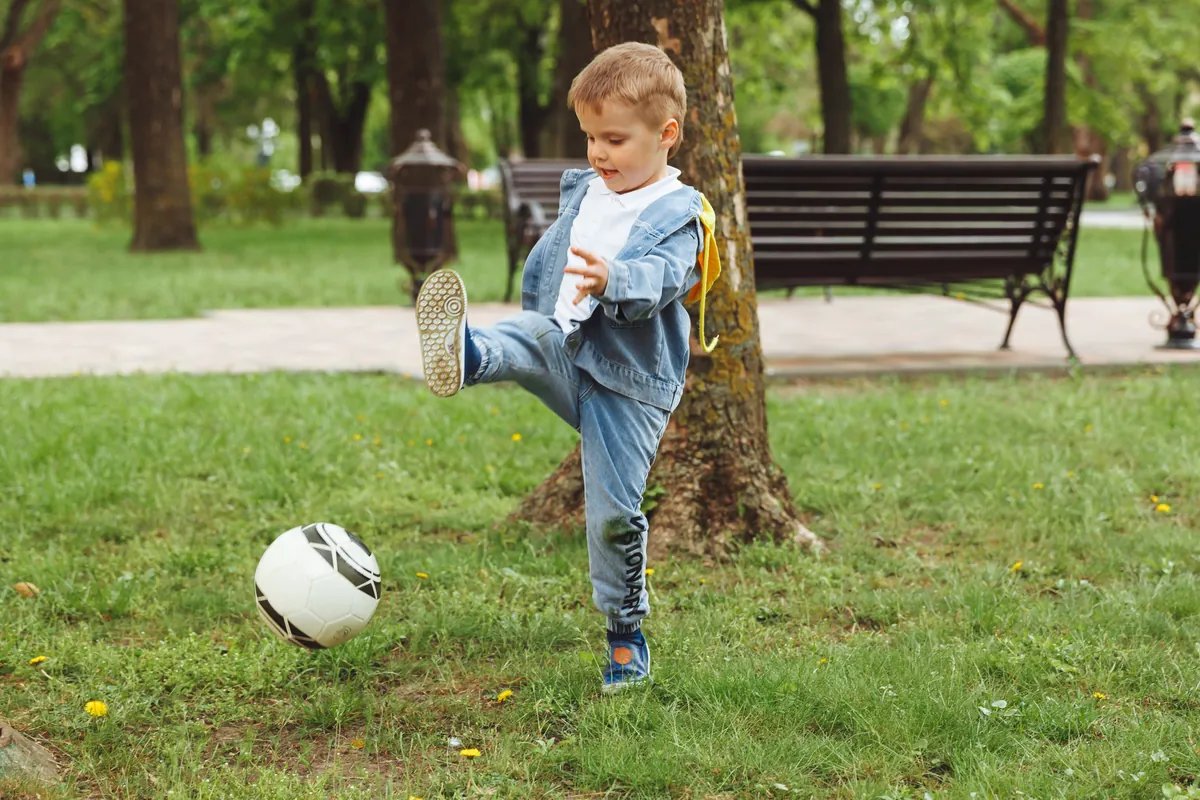 When do babies learn to kick a ball?